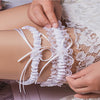 Ivory lace bowknot bridal garter set being applied to a person's leg.