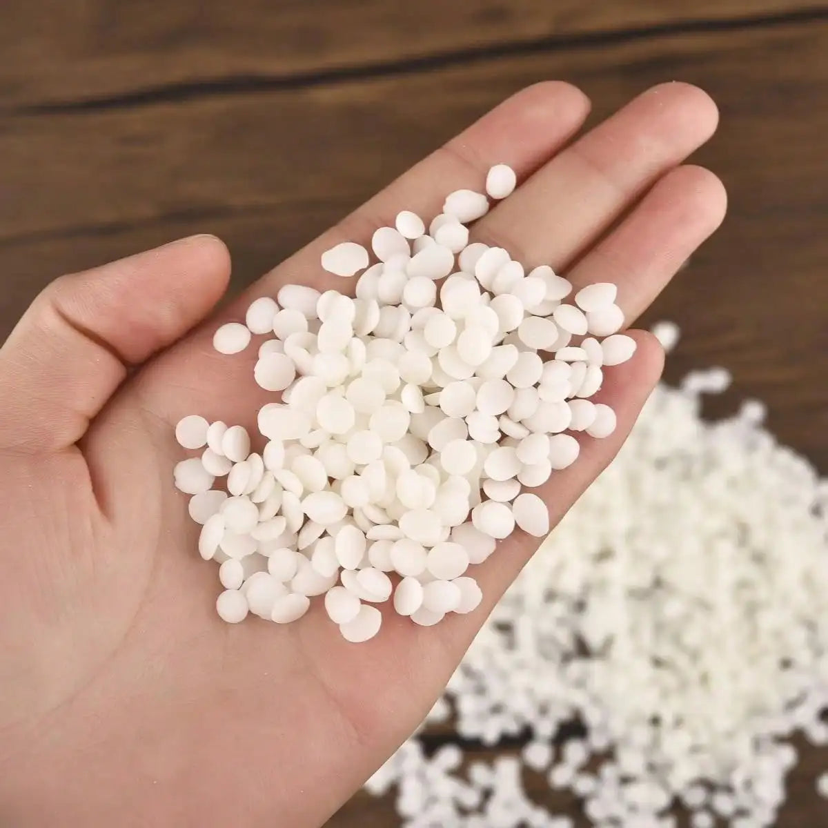 A hand holds a pile of white natural soy wax flakes for DIY candle making.