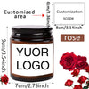 A dark glass jar candle with a white label featuring the text YOUR LOGO and a rose scent, shown next to fresh red roses.