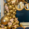 A large balloon garland made of metallic gold and bronze balloons decorated with pink floral accents against a dark blue back