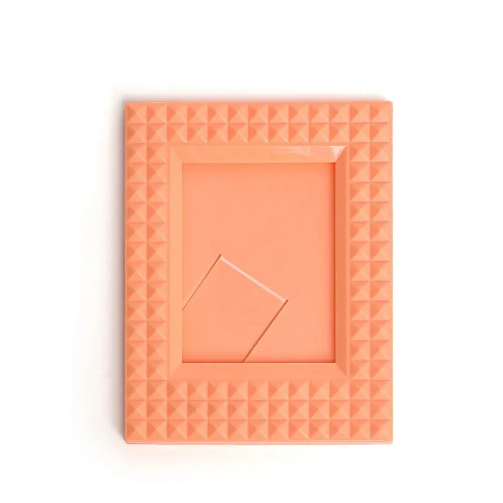 A square orange mini film frame with a textured, geometric border and a central opening.