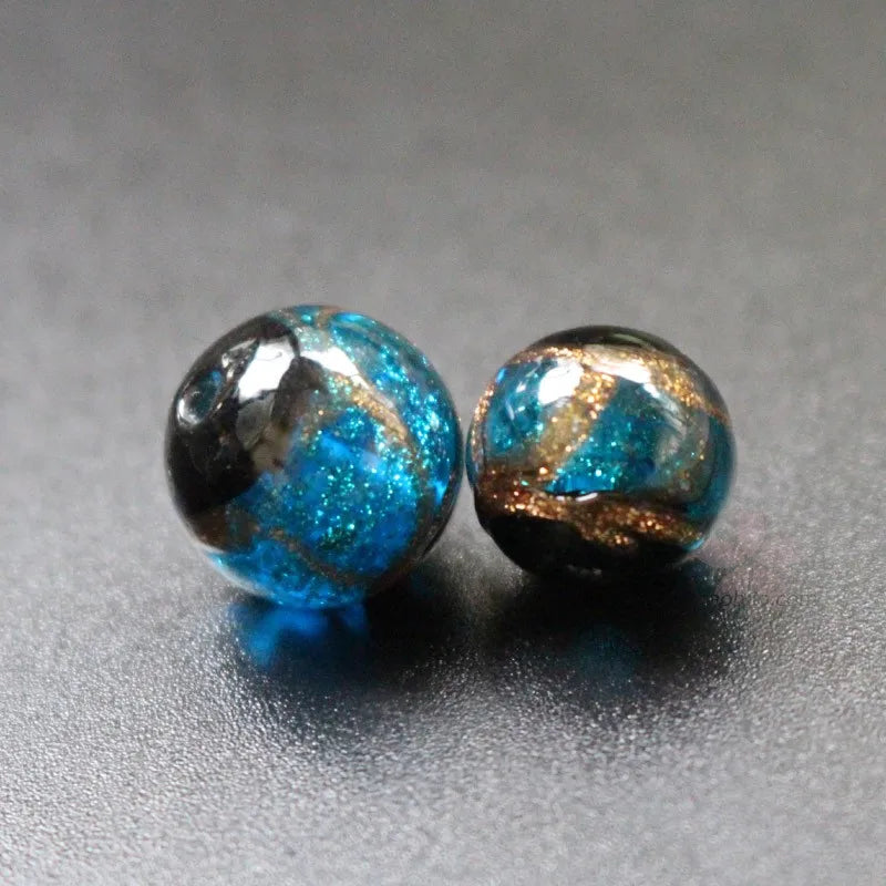 Two handcrafted lampwork glass beads with blue and gold accents resting on a gray surface.