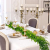 Une table blanche décorée de guirlandes d'eucalyptus artificiel et de chandeliers dorés.