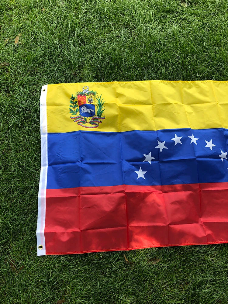 A large Venezuelan national flag banner featuring yellow, blue, and red stripes with a coat of arms and stars on a green lawn