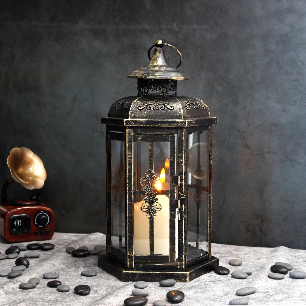 A vintage Nordic iron candle lantern with glass panes sits on a gray cloth surrounded by smooth dark stones.