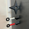 A black refrigerator ornament shaped like a dart, featuring a hexagonal opening and two white and red darts.