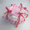 A pink decorative fake cake with piped frosting and red gingham ribbons on a clear stand.