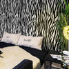 A bedroom setting featuring a black and white zebra print wall, pillows with text, and green foliage.