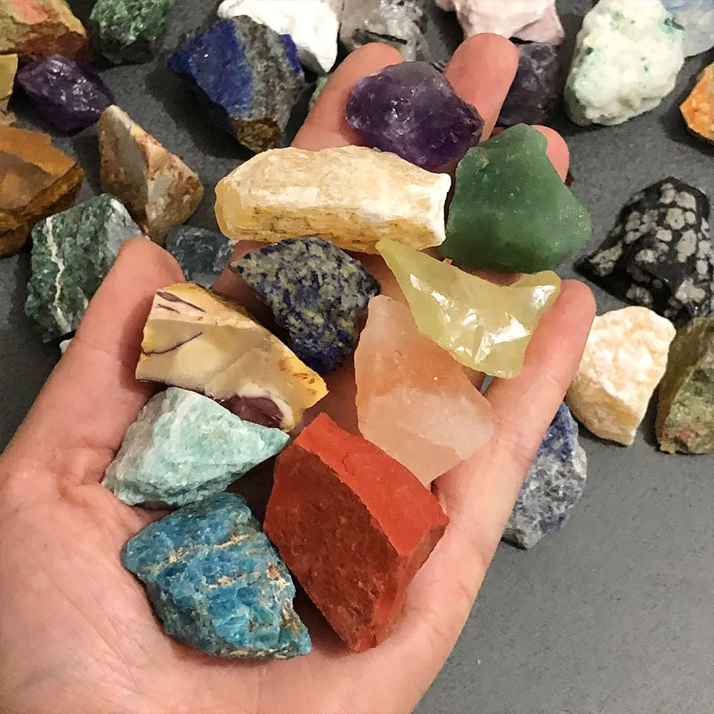 A hand holds an assortment of mixed natural raw crystal stones and healing minerals in various colors and shapes.