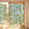 A close-up view of a window with decorative privacy film featuring green leaves and white background.