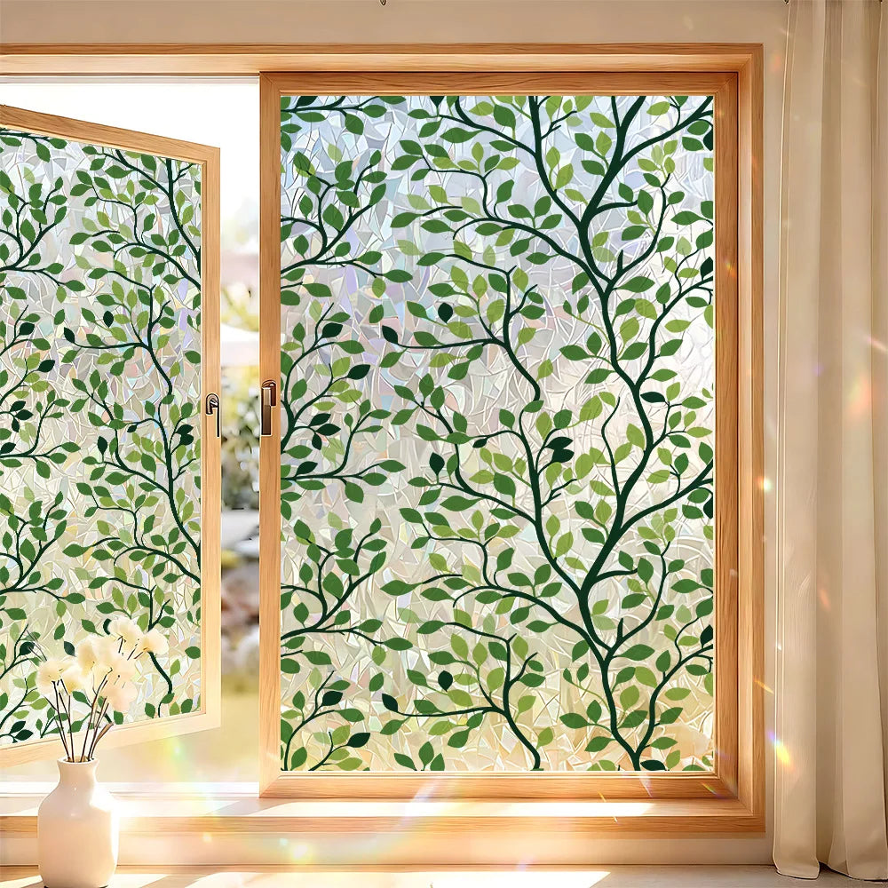 A close-up view of a window with decorative privacy film featuring green leaves and white background.