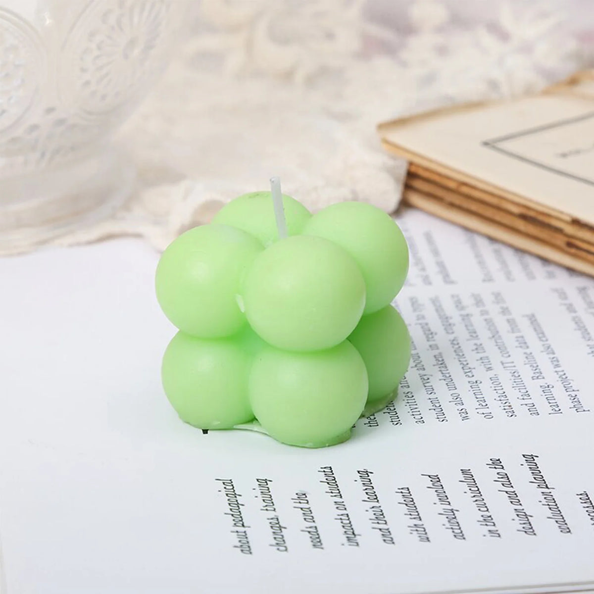A set of two light green cube soy wax candles resting on a white surface next to a notebook.