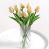 A bouquet of light yellow artificial tulips in a clear glass vase on a white plate.