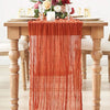 A semi-sheer orange table runner draped over a wooden table with floral arrangements.