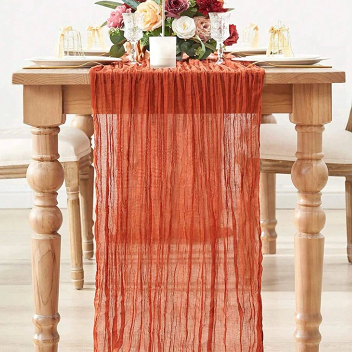 A semi-sheer orange table runner draped over a wooden table with floral arrangements.
