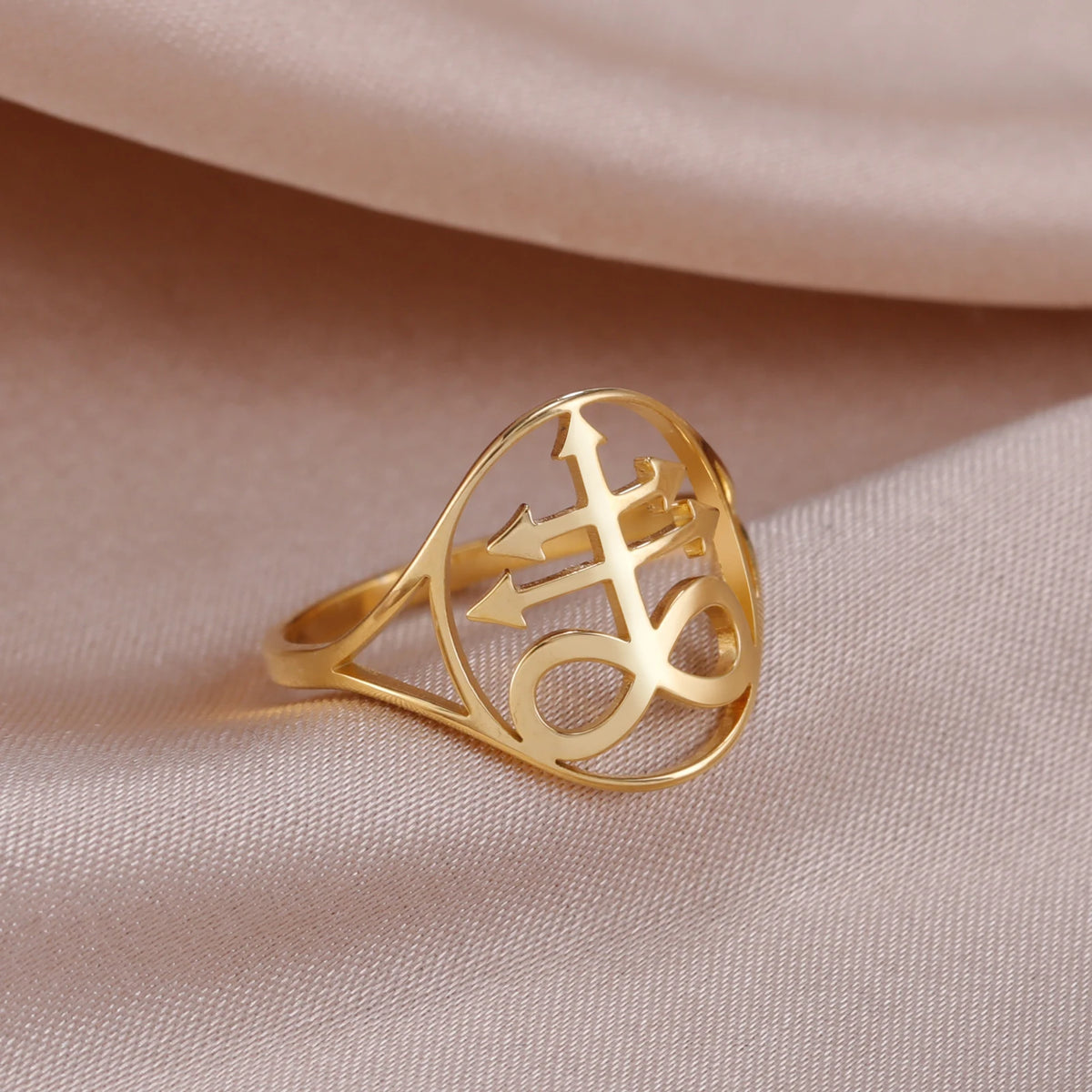 A gold signet ring featuring a Leviathan cross design, resting on a soft beige fabric.