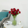 Un ramo de rosas artificiales de seda rojo intenso en un jarrón de vidrio transparente sobre una mesa blanca.