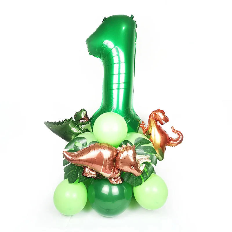 A green foil number one balloon surrounded by green leaves and a gold dinosaur figurine.