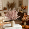 A vase filled with pink artificial silk lover grass on a white marble table in a warmly decorated room.
