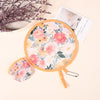 A pink floral patterned portable foldable cooling handheld fan with a wooden handle and a matching card.