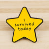 A yellow star enamel pin with black outline featuring the text I survived today.