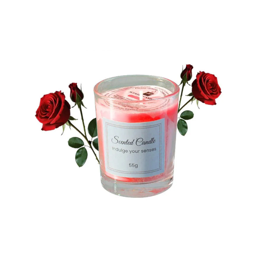 A glass jar candle with pink wax and a label, surrounded by red roses.
