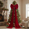An elegant velvet Christmas tree topper bow with long red streamers adorning a decorated Christmas tree.