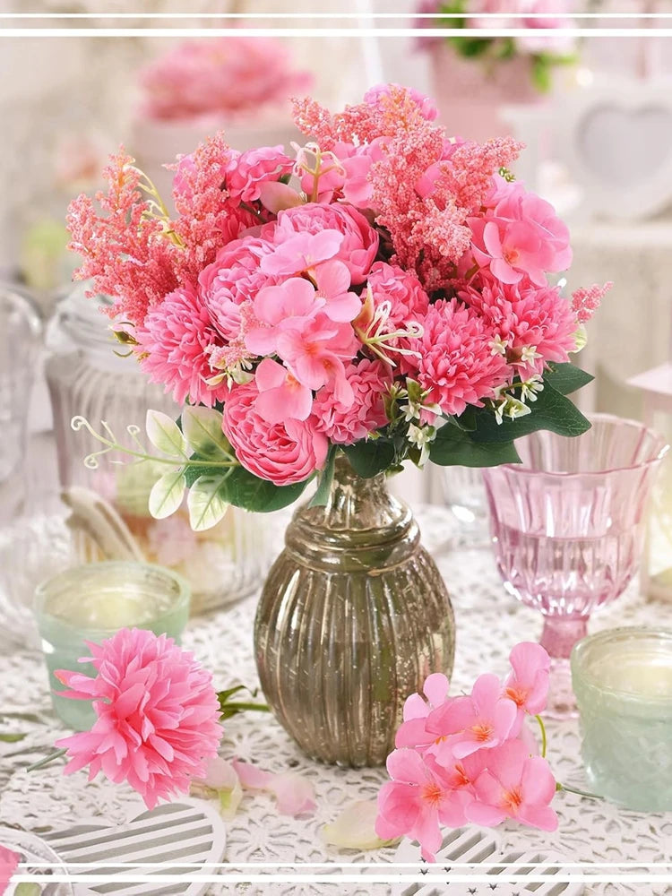 A bouquet of pink and coral artificial silk peony flowers in a gold vase on a white lace tablecloth.