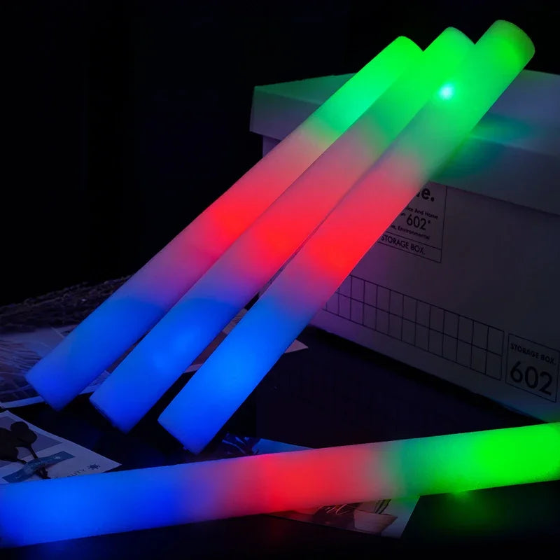 A bundle of glowing RGB foam sticks in blue, red, and green light lying on a dark surface.