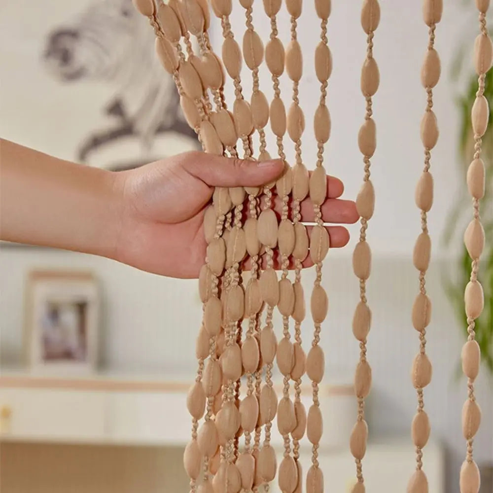 A hand is touching an elegant beaded string curtain with tassels used as a bohemian door and window drape.