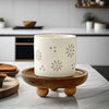 A white ceramic candle in a natural wood tray on a marble surface.