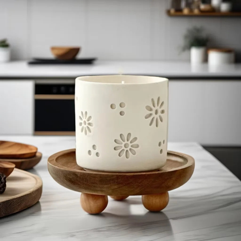 A white ceramic candle in a natural wood tray on a marble surface.