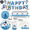 A set of blue shark foil balloons and decorations including a banner, a plate, a table runner, and a paper fan.