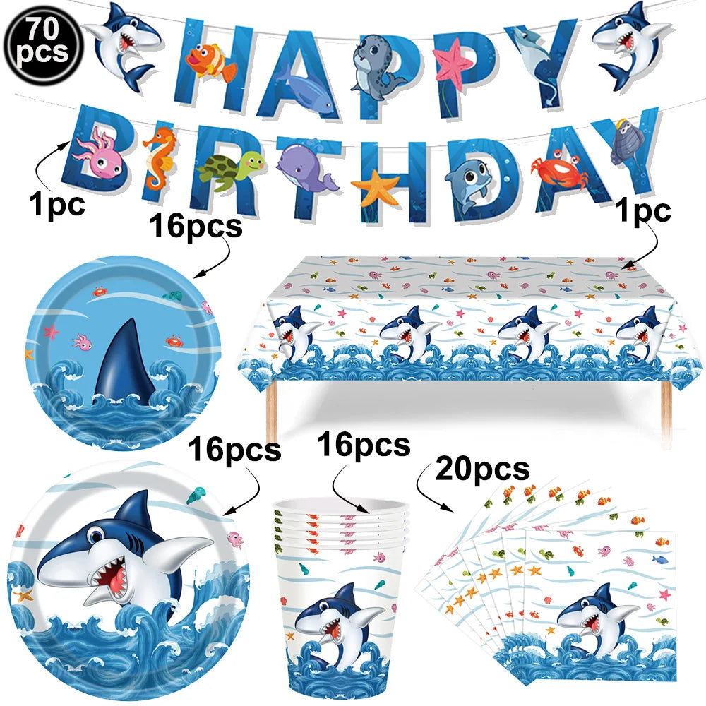 A set of blue shark foil balloons and decorations including a banner, a plate, a table runner, and a paper fan.