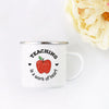 A white enamel mug with black text that reads Teaching is a work of heart, set against a white background and a yellow floral