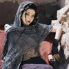 A female model wearing a dark gray hooded cloak with intricate detailing and a gold Viking brooch.