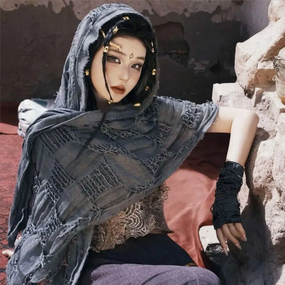 A female model wearing a dark gray hooded cloak with intricate detailing and a gold Viking brooch.