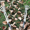 A pair of realistic skeleton hand lawn stakes used for Halloween graveyard decor are lying on green grass amidst fallen autum