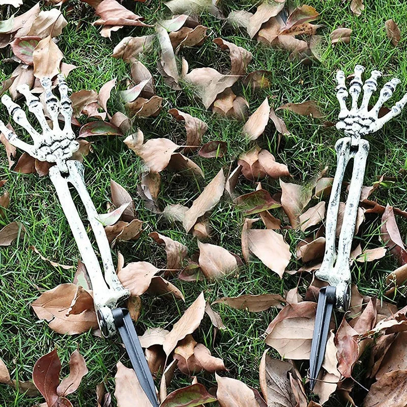 A pair of realistic skeleton hand lawn stakes used for Halloween graveyard decor are lying on green grass amidst fallen autum
