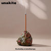 A wooden stick is placed into a rough, reddish-green crystal on a neutral background.