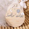 A wooden birth announcement sign featuring a crescent moon, stars, and the words hello world on a light wood background.