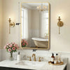 A modern wall mirror with a gold metal frame reflecting a bathroom interior and a bathtub.