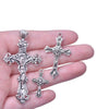A hand holds several antique silver cross charms for jewelry making