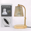 A brass adjustable electric candle warmer lamp with a glass shade and wooden base.