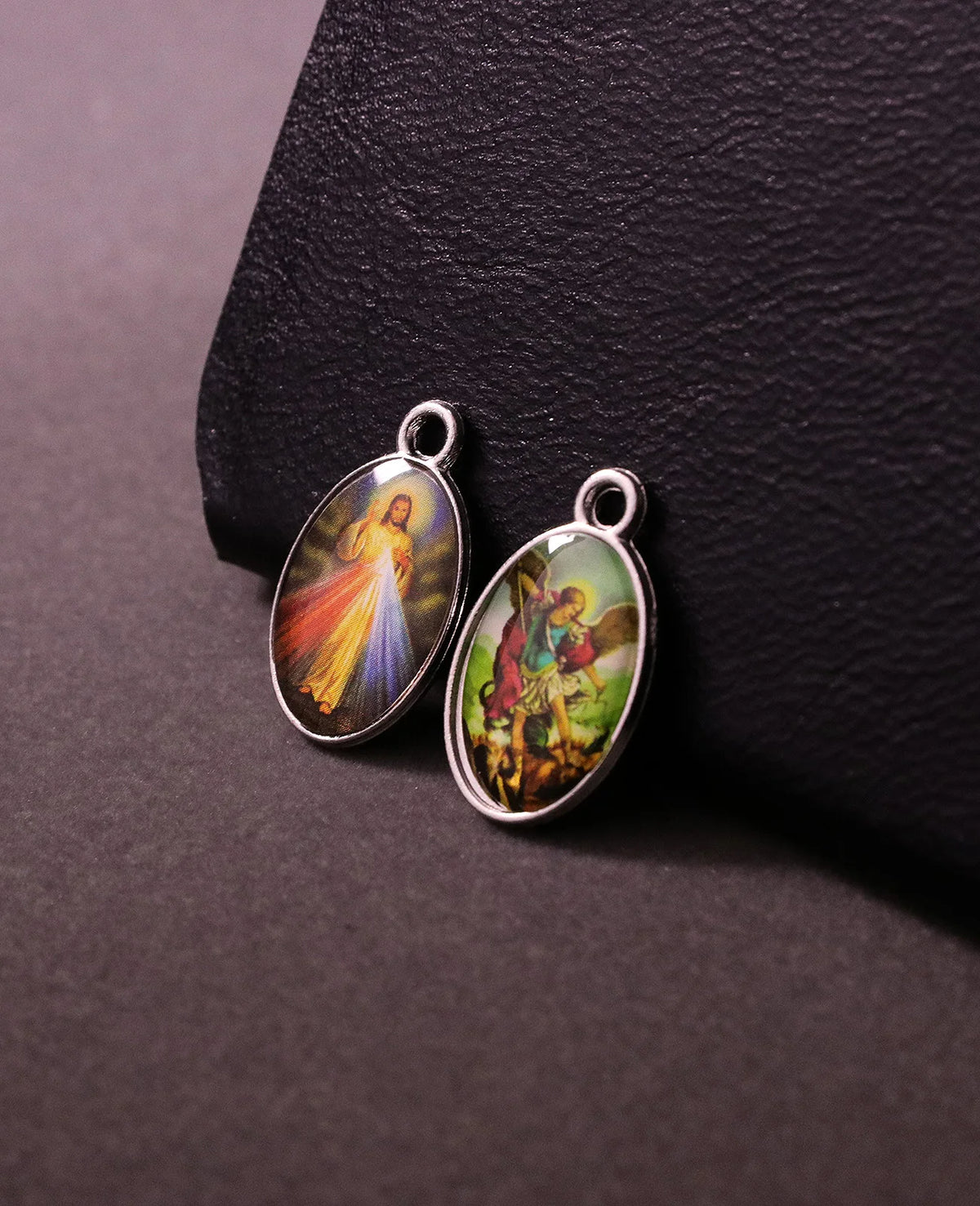 Deux pendentifs argentés représentant des scènes religieuses, incluant Jésus et Saint Michel.