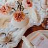 A close-up of a floral arrangement and a semi-sheer gauze table runner in sage green on a wooden surface.