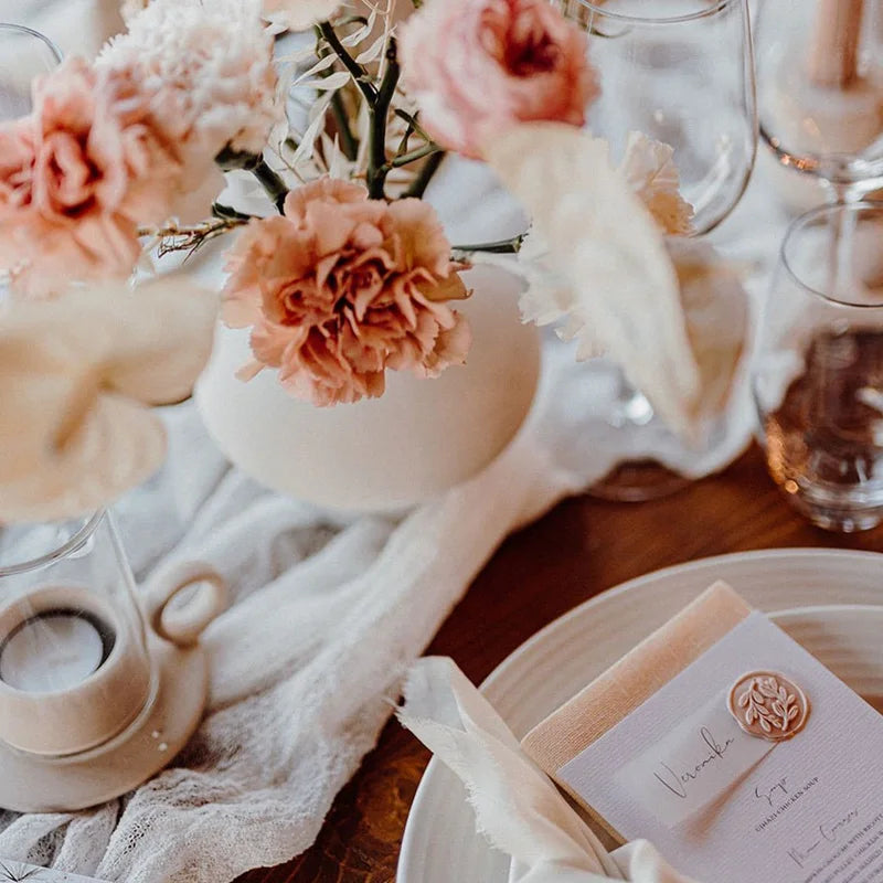 A close-up of a floral arrangement and a semi-sheer gauze table runner in sage green on a wooden surface.