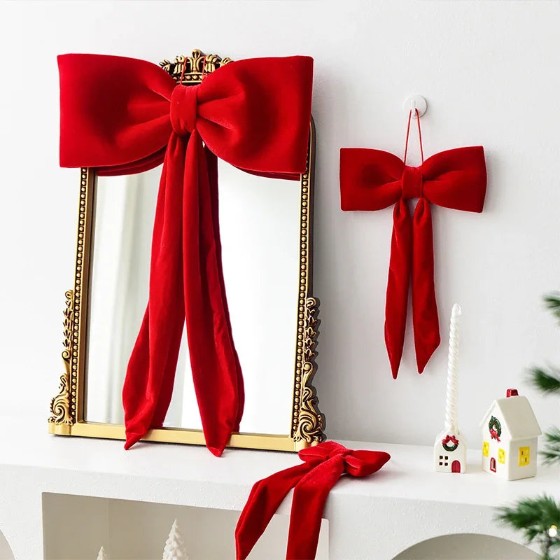 A set of twelve red velvet Christmas tree bow ornaments displayed next to a gold-framed mirror.