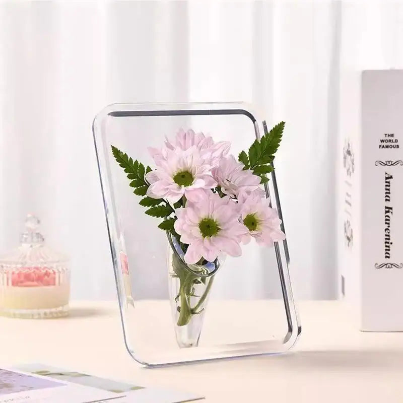 A clear acrylic frame flower vase holding pink flowers and green leaves for modern home decor.