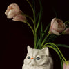 A white ceramic cat sculpture with pink tulips emerging from its head.